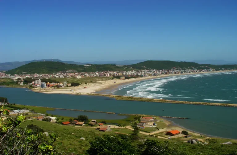 Vista deslumbrante da Praia do Mar Grosso em Laguna, com suas águas calmas e areia dourada, rodeada por um cenário natural encantador